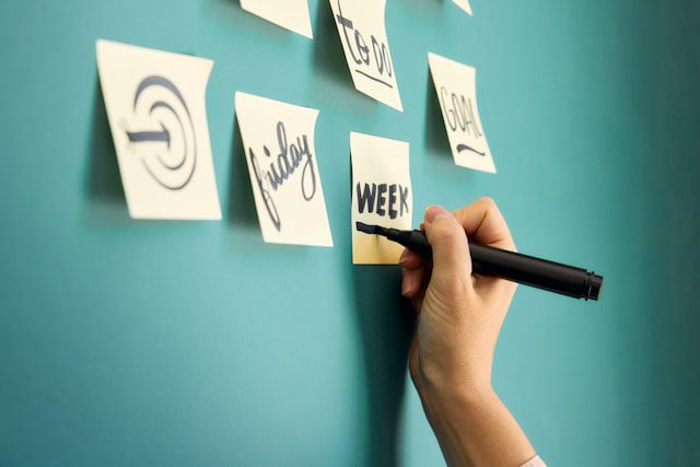 Hand writing on sticky notes with various words displayed on a wall in the background.