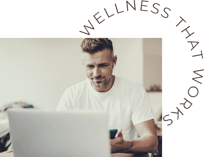 Man with earbuds smiles while working on a laptop, suggesting engagement and productivity. Relevant for wellness-related content.
