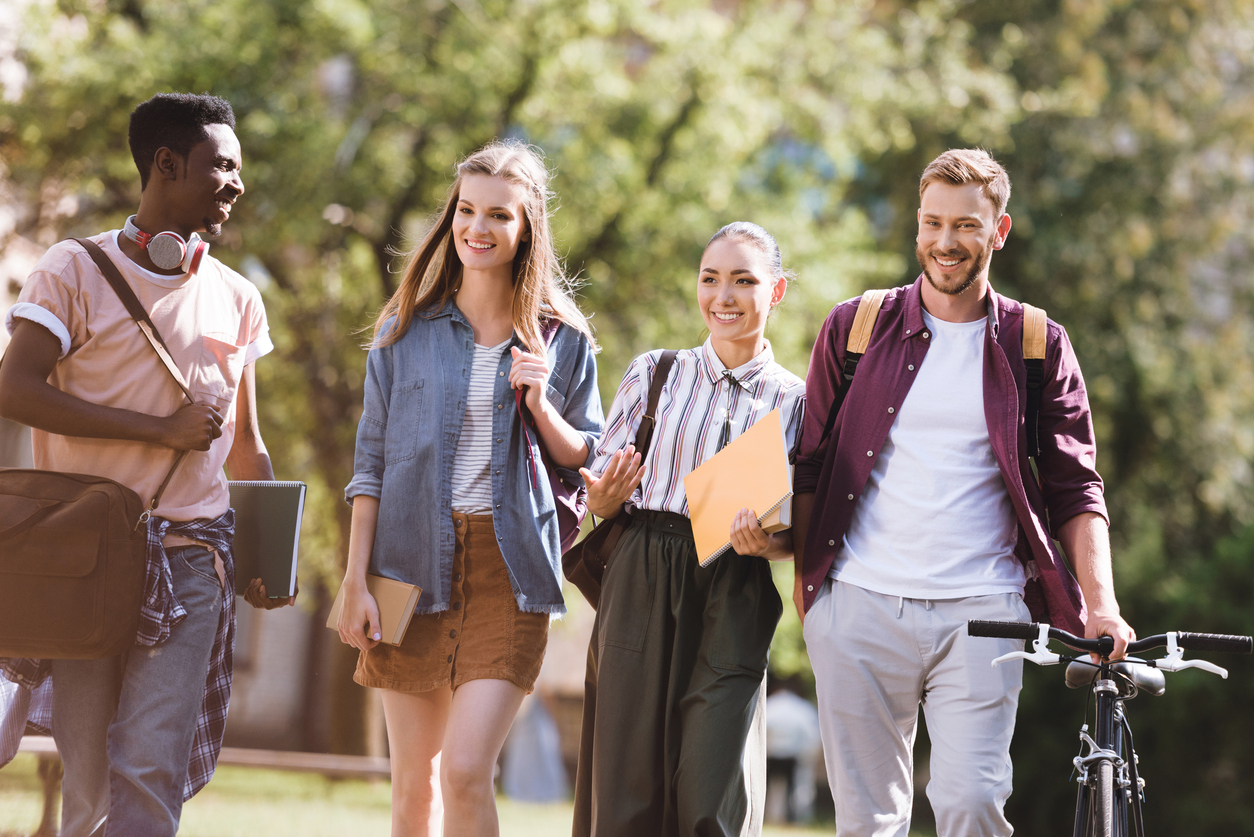 group of smiling multicultural students spending time together in park